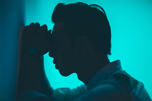Φωτογραφία σε μπλε χρώματα ενός ατόμου από το πλάι, ακουμπισμένο με τα χέρια και το πρόσωπο προς έναν τοίχο