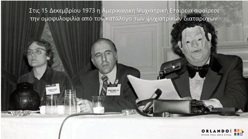Ο Jonh Fryer μιλάει φορώντας μάσκα στο ετησιο συνέδριο της Αμερικανικης Ψυχιατρικής εταιρείας. Στο πάνω μέρος της εικόνας, η φράση "Στις 15 Δεκεμβρίου 1973 η αμερικανικη ψυχιατρική εταιρεία αφαίρεσε την ομοφυλοφιλία από τον κατάλογο των ψυχιατρικών διαταραχών". Κάτω αριστερά το λογοτυπο του orlando lgbt+